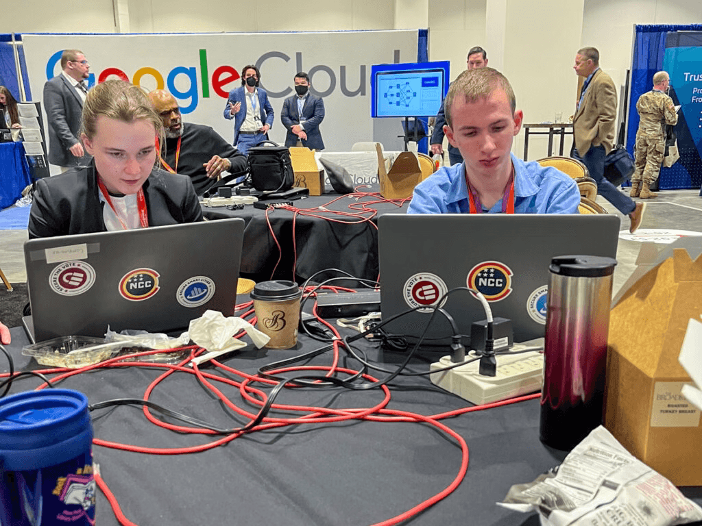 Two cybersecurity students working at laptops during a hands-on training event.