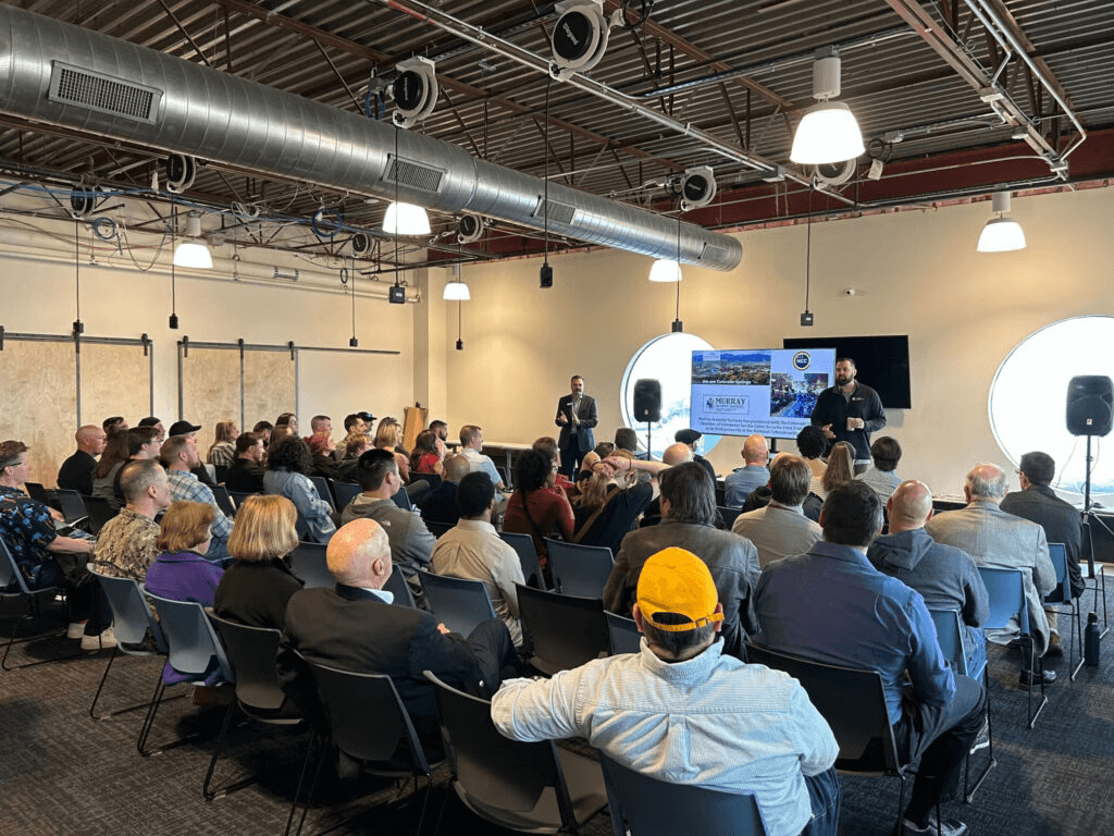 Audience seated at an NCC event with a speaker presenting at the front of the room.